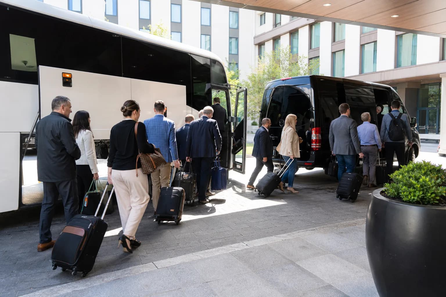Business group with luggage boarding a coach outside a modern glass building