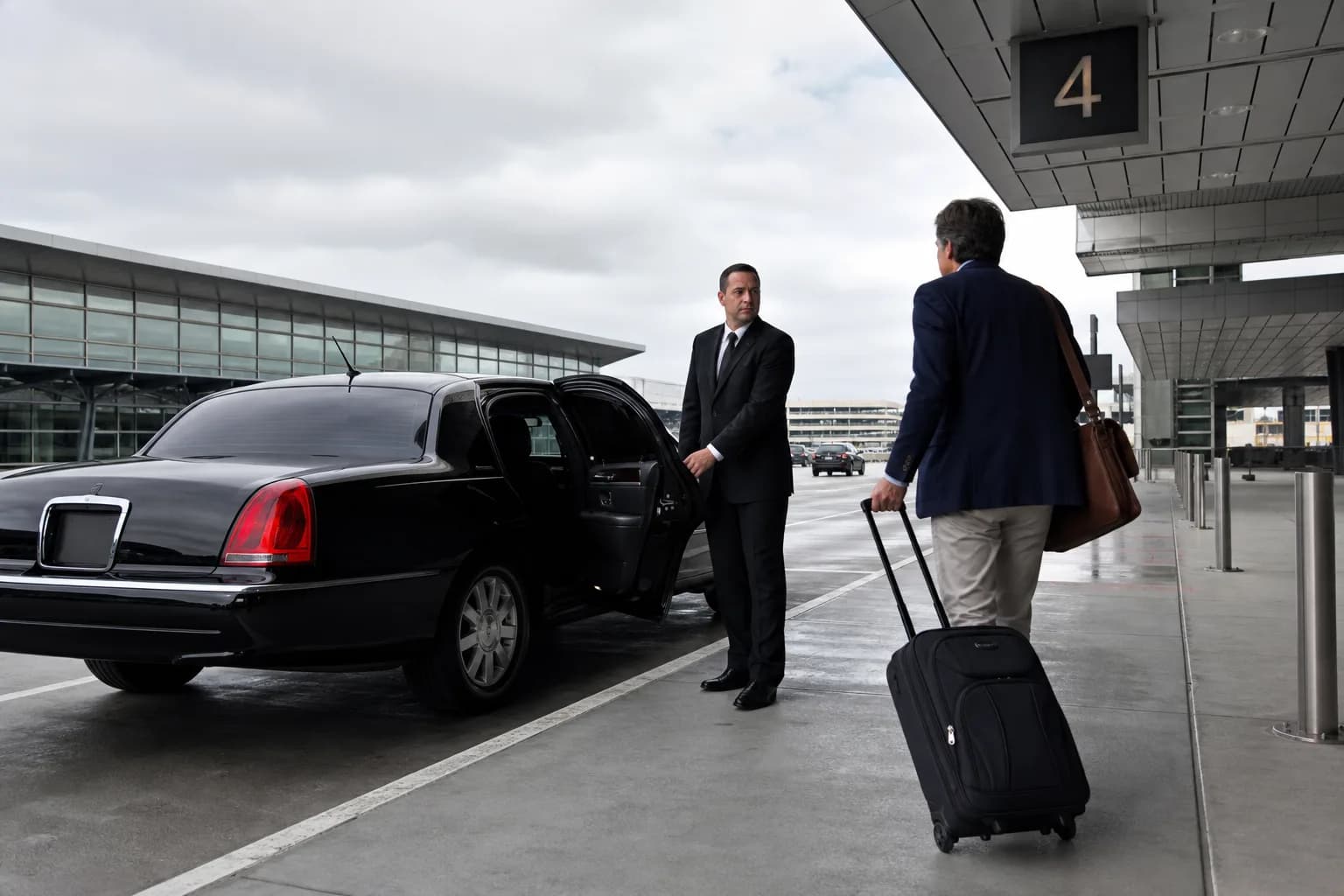 Chauffeur meeting a traveller with a suitcase beside a black limousine at an airport curb