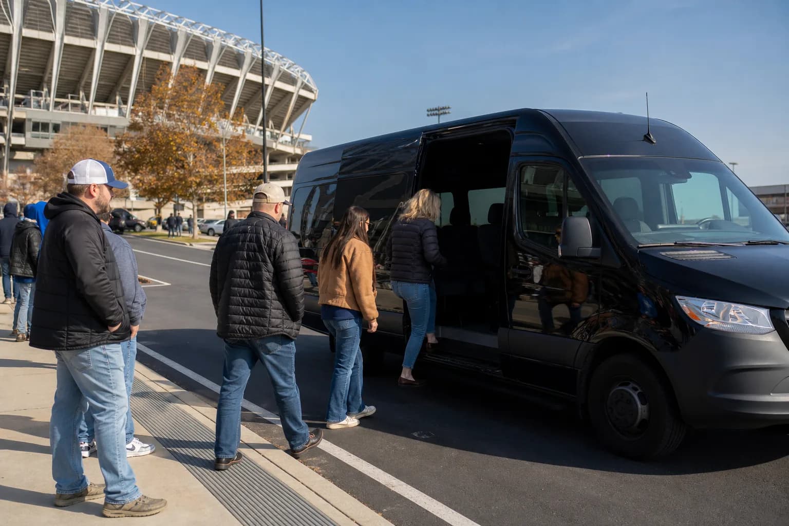 Black sprinter van waiting at a stadium crosswalk as people cross the street